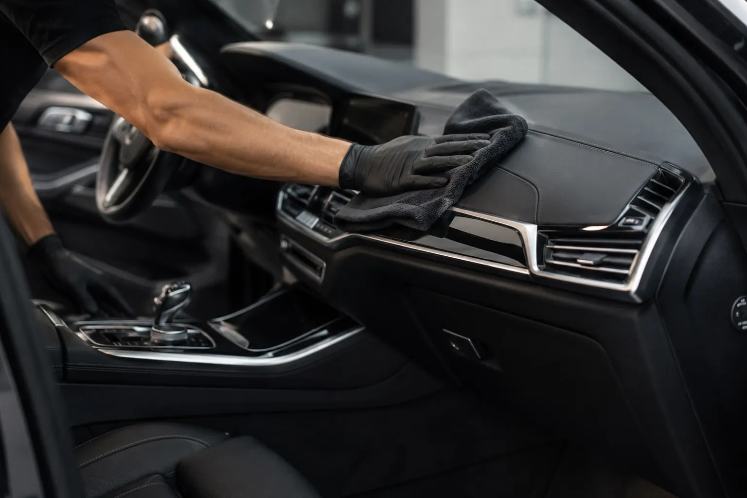 Main gantée essuyant le tableau de bord d’une voiture avec une microfibre